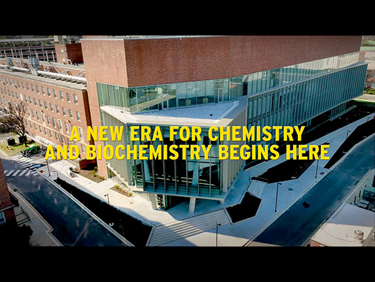 Letterboxed video still from the opening of a video showing the new chemistry building overlaid with the words A New Era for Chemistry and Biochemistry Begins Here
