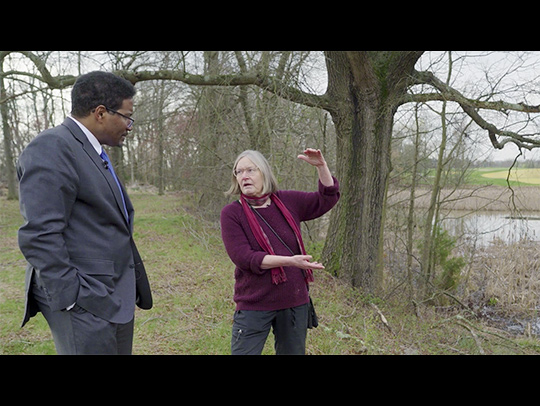 A letterboxed video still of UMD President Darryll Pines with Professor Karen Prestegaard standing on a grassy hill overlooking the UMD golf course