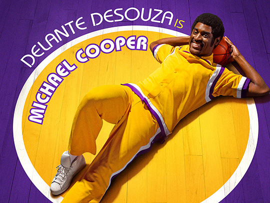 A promotional photo of Delante Desouza (B.S. 16) laying on a purple and gold basketball court, in costume as NBA shooting guard Michael Cooper for the HBO series Winning Time-The Rise of the Lakers